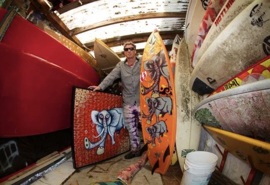 Shawn Barney Barron in his shed with an elephant painting and his orange elephant surfboard.